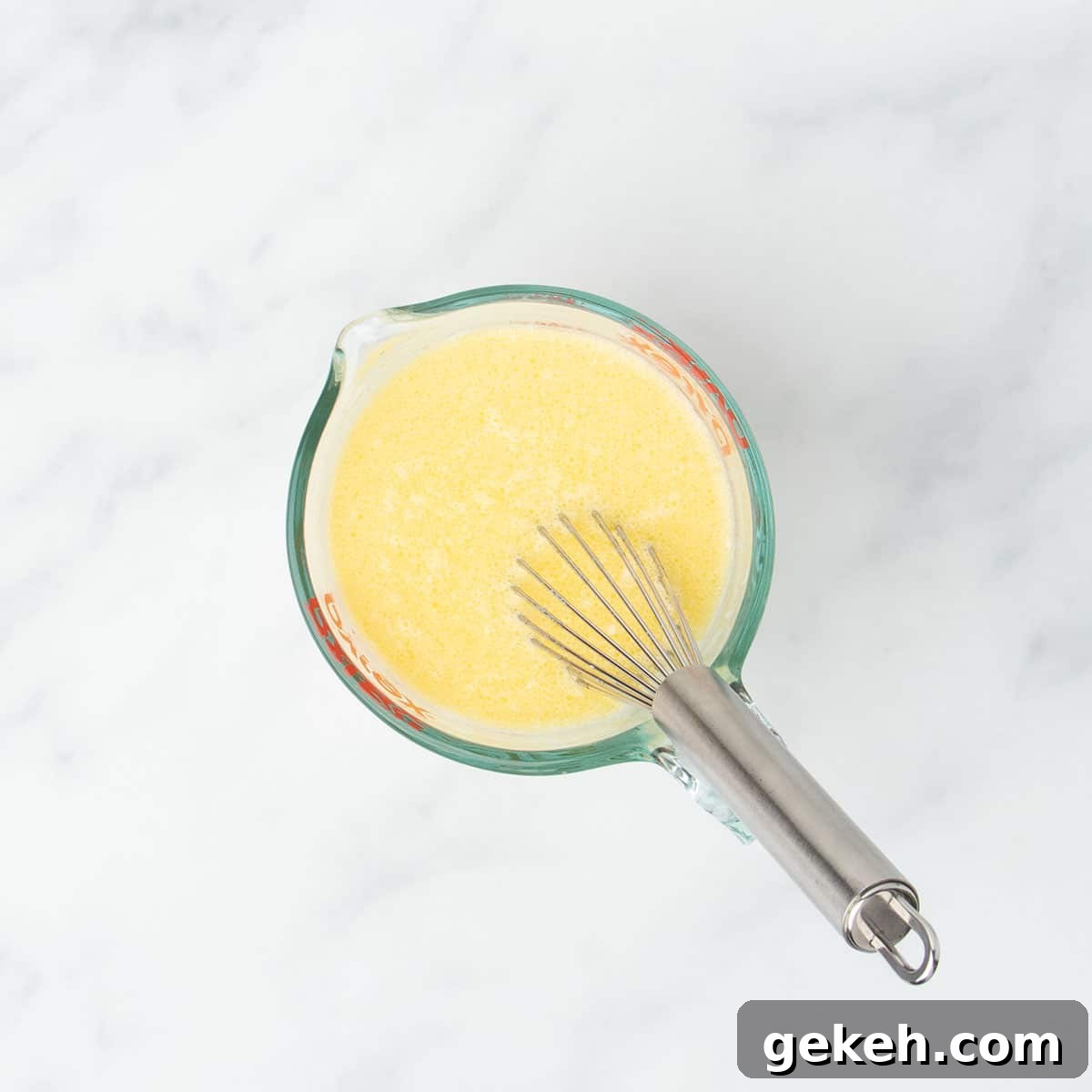 2 cup glass measuring cup with yellow whisked mixture and metal wire whisk in cup