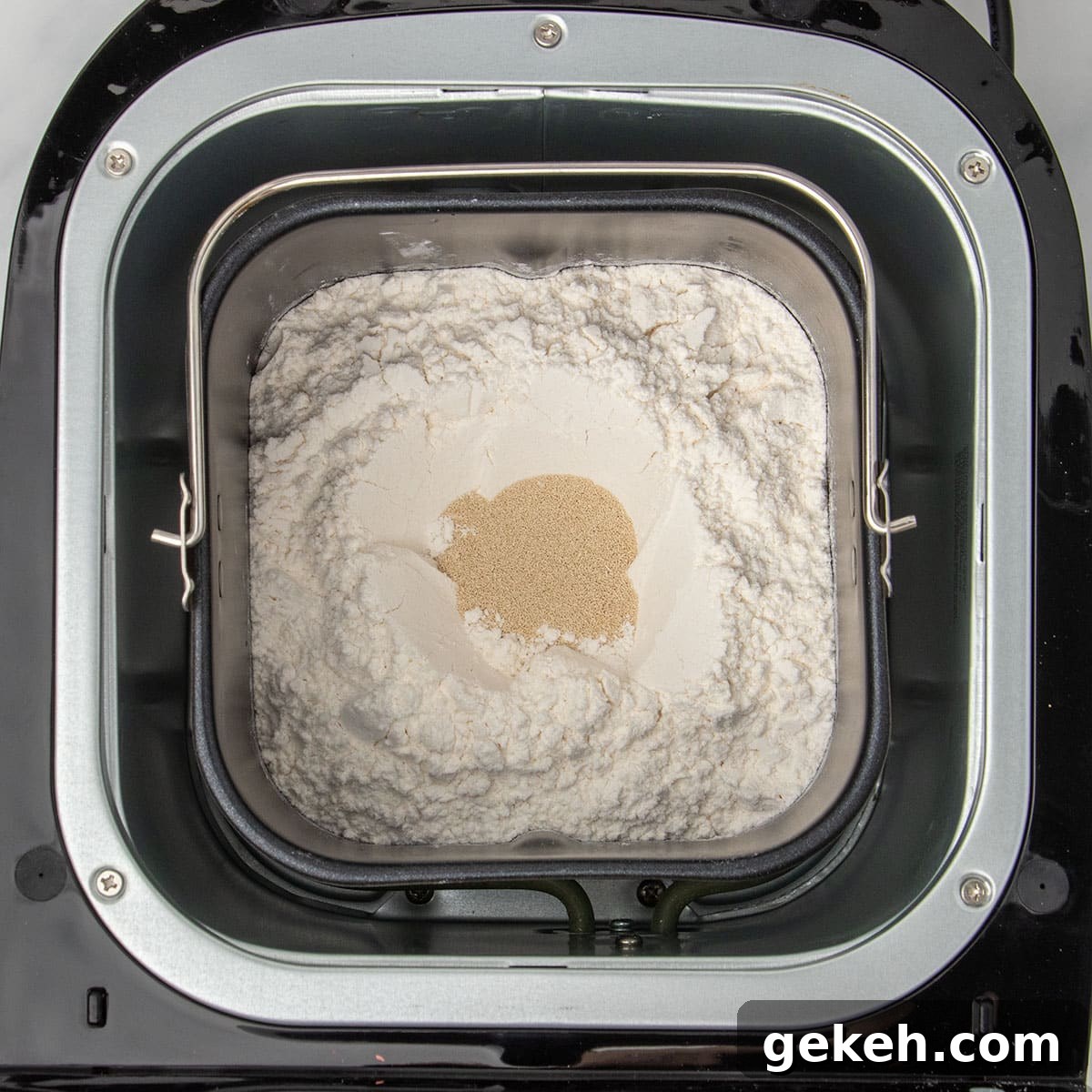 same baking pan with flour on top and instant yeast granules in small hole in center of flour in baking pan in bread machine