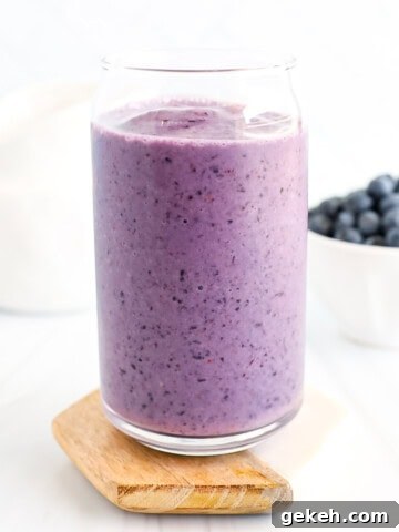 A blueberry smoothie in a clear cup.