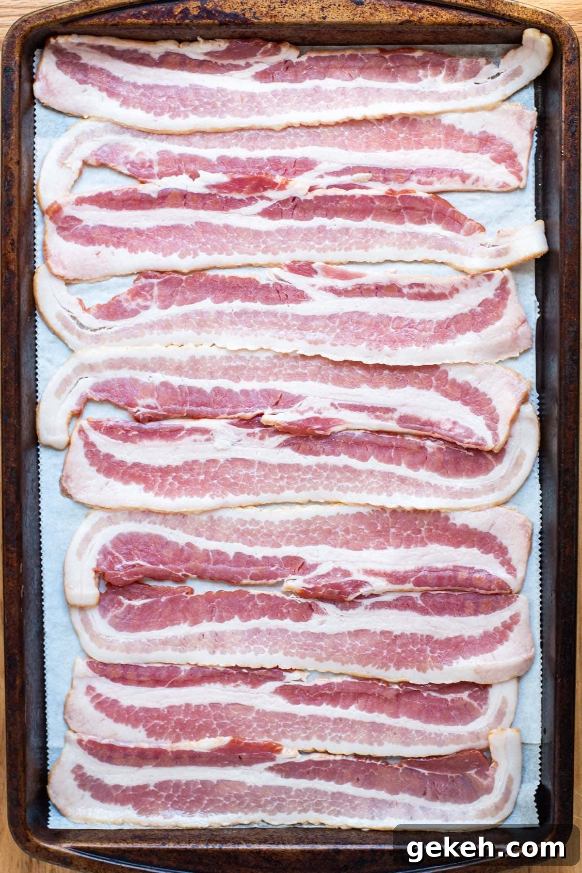 Perfectly Crispy Oven-Baked Bacon: Simple Sheet-Pan Method 4 Raw, uncooked bacon on a baking sheet lined with parchment paper.