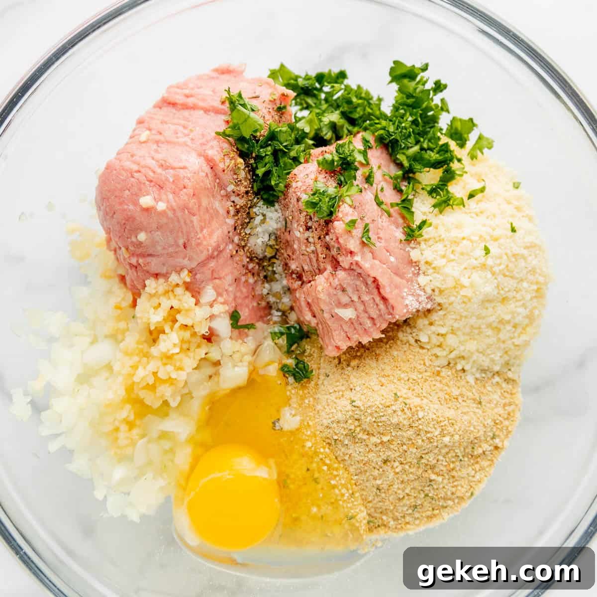 Bowl with ground meat, chopped onions, minced garlic, breadcrumbs, a raw egg, and chopped parsley.