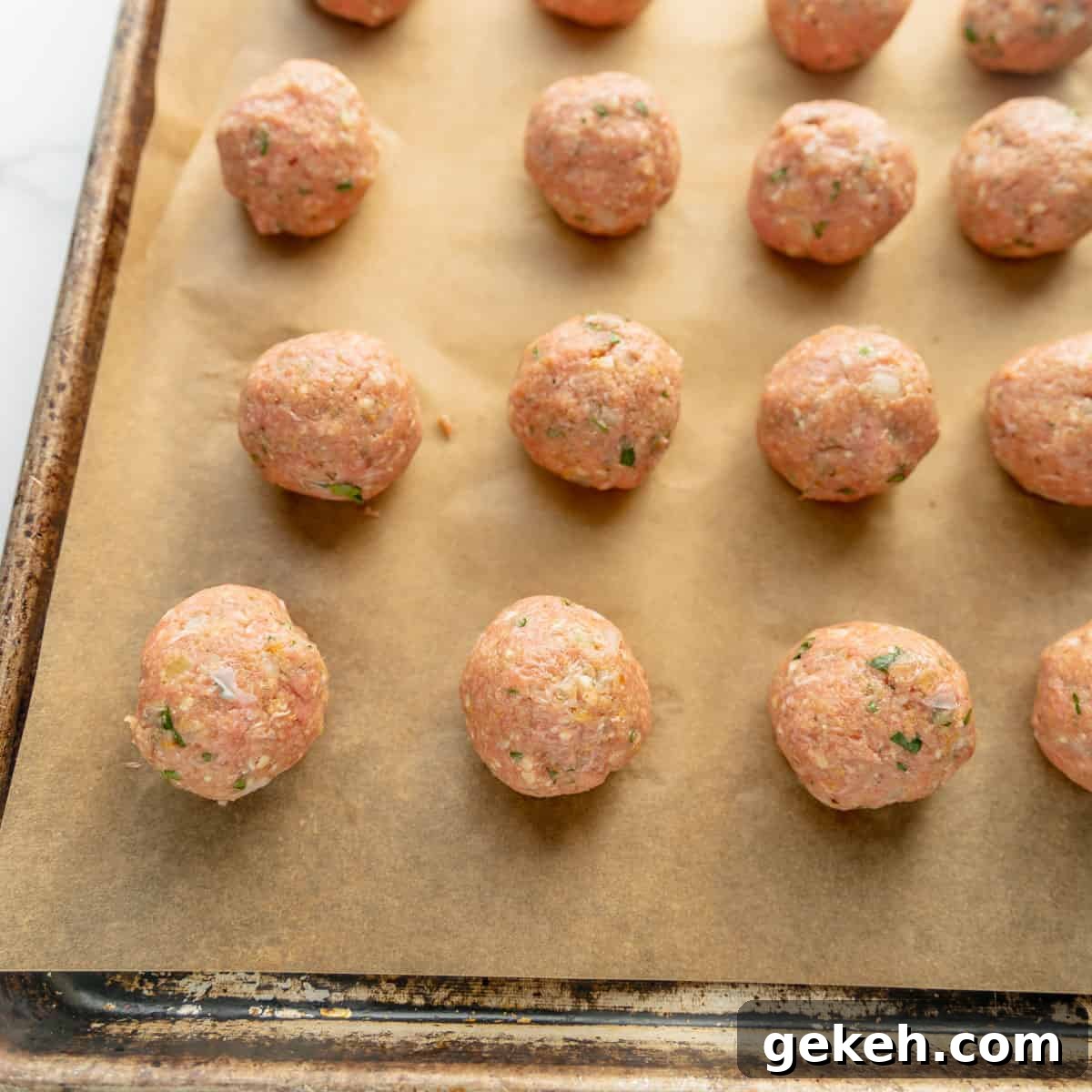 Raw meatballs with herbs on a parchment-lined baking sheet, ready for cooking.