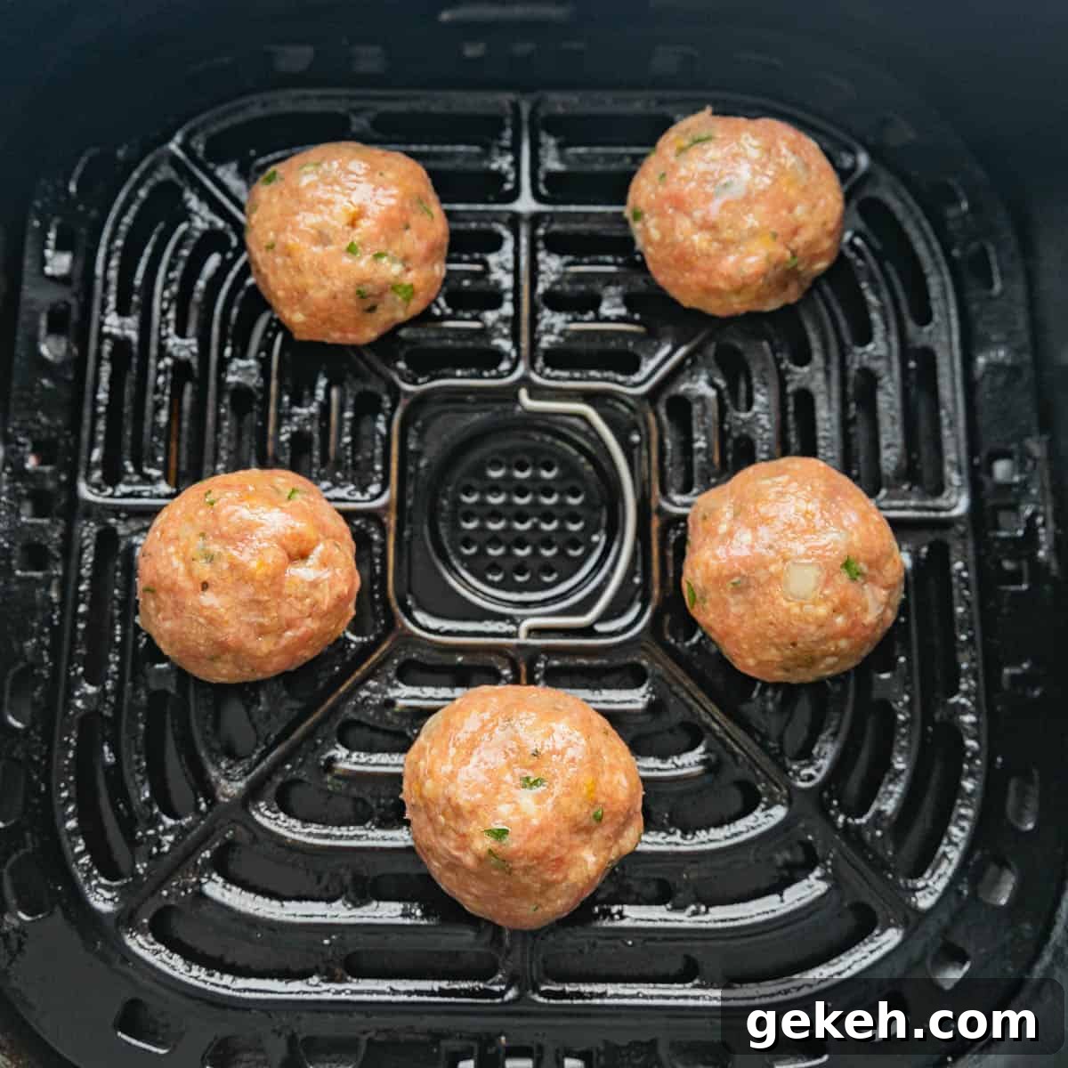 Five uncooked meatballs arranged in an air fryer basket.
