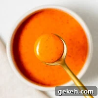 Spicy Gochujang Mayonnaise Sauce Recipe 8 A small white ceramic bowl with bright orange gochujang mayo and a golden serving spoon.