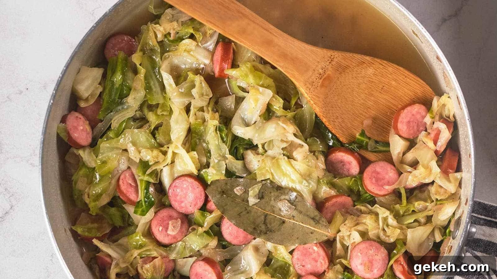 15 Sophisticated Dinner Ideas to Impress with Minimal Effort 16 A pan filled with fried cabbage and sausage, with a wooden spoon resting inside.