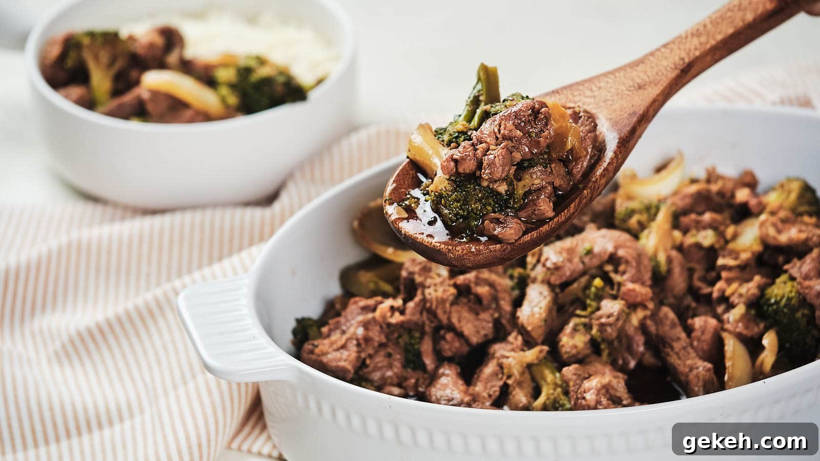 15 Sophisticated Dinner Ideas to Impress with Minimal Effort 10 A wooden spoon serving beef and broccoli from a white baking dish, with a side of rice visible in the background.
