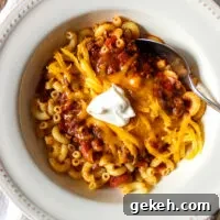Bowl of chili over macaroni with toppings.