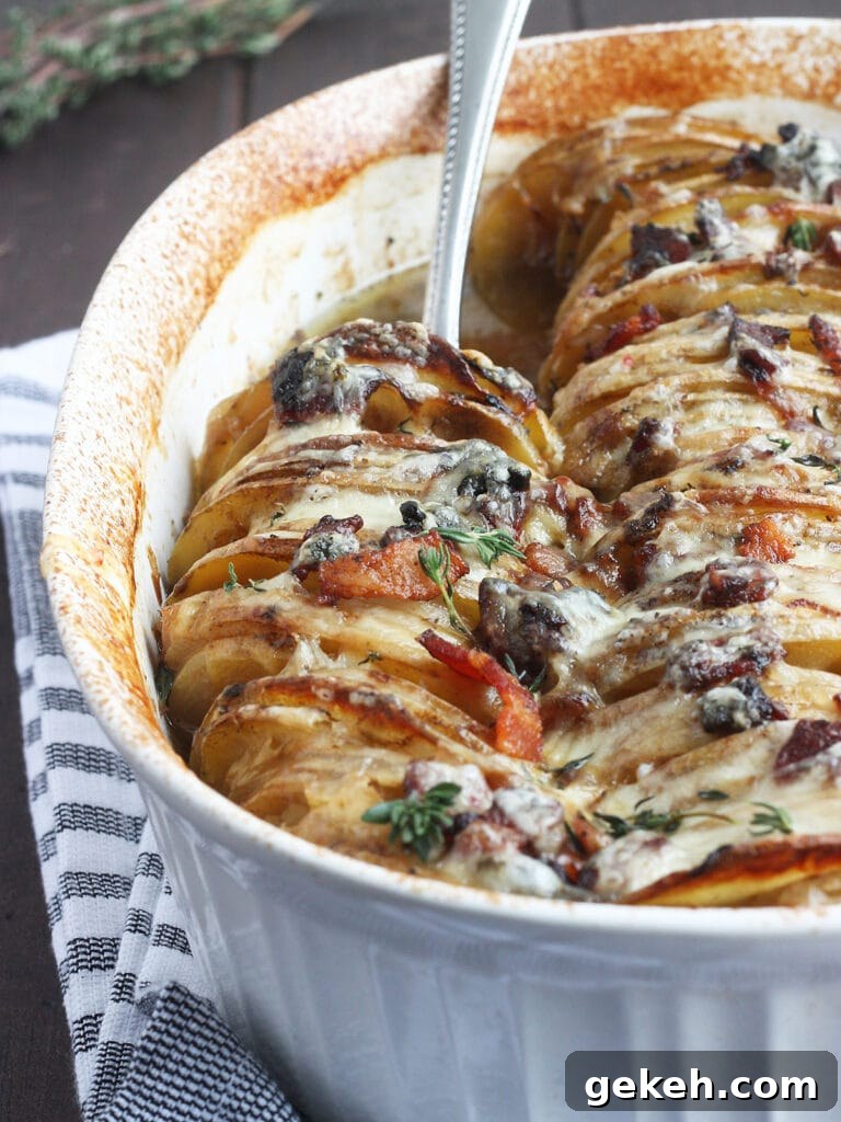 Creamy Scalloped Potatoes with Crispy Bacon 24 Metal spoon scooping out a serving of scalloped potatoes with bacon from a white oval casserole dish.