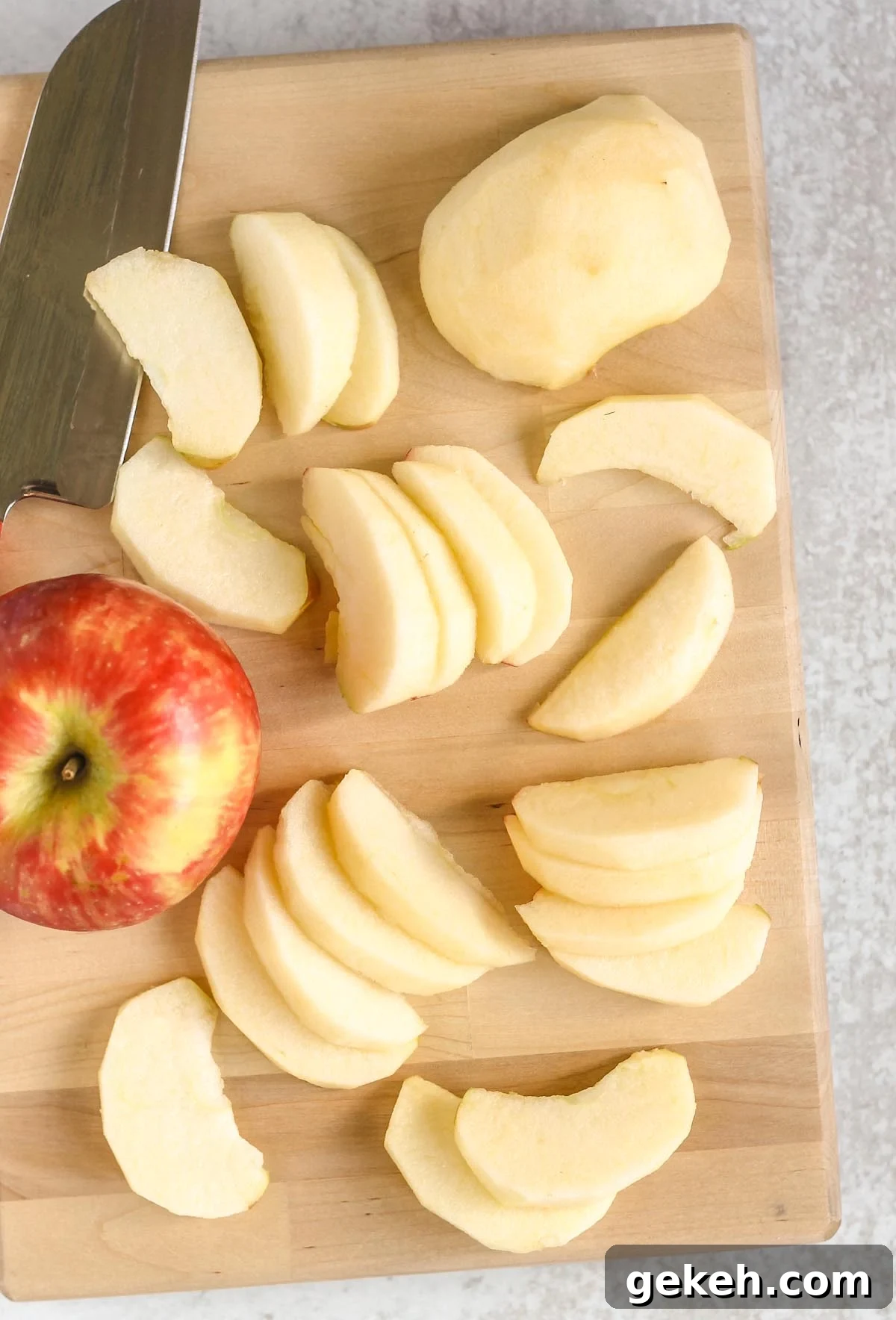 Peeled and sliced apples on a cutting board with a knife and a whole apple on the side.