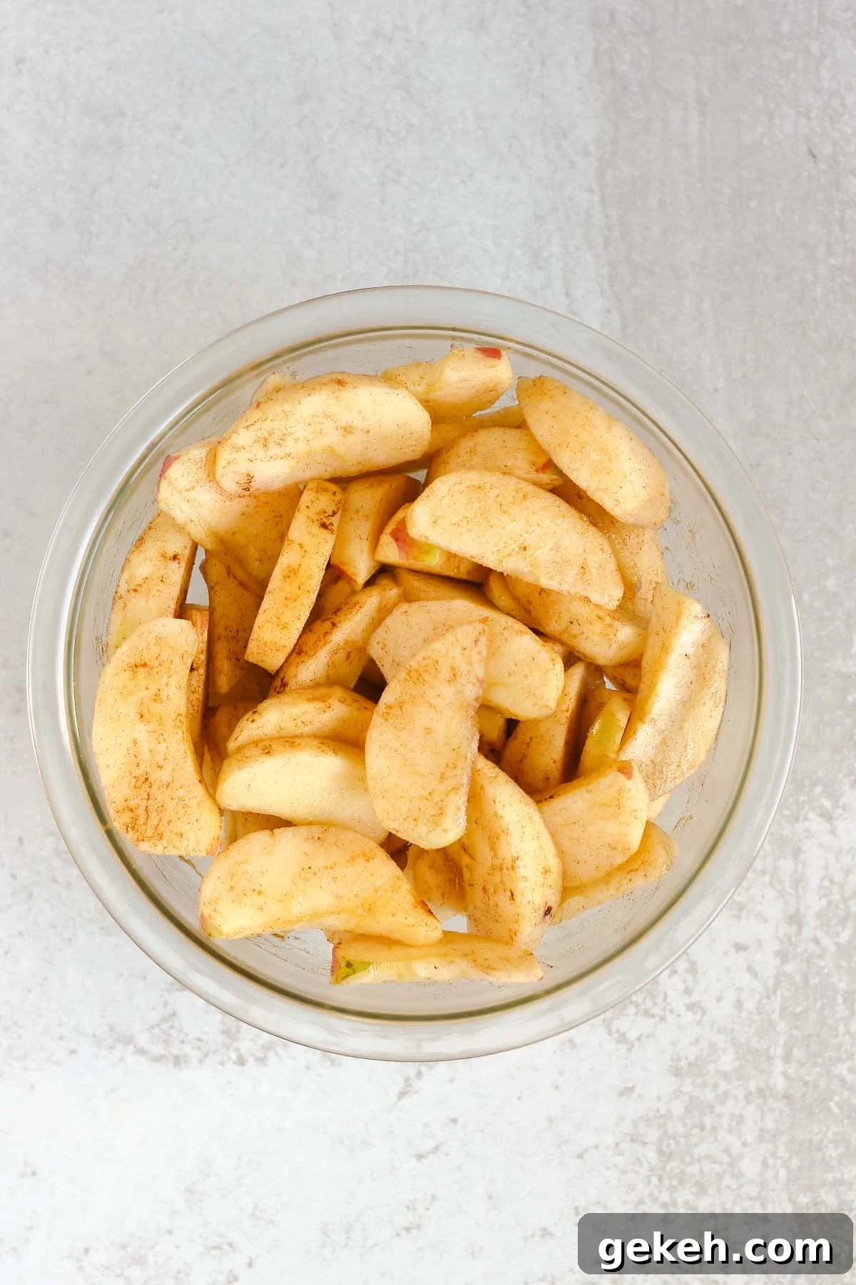 Apple slices mixed with cinnamon in a glass mixing bowl.