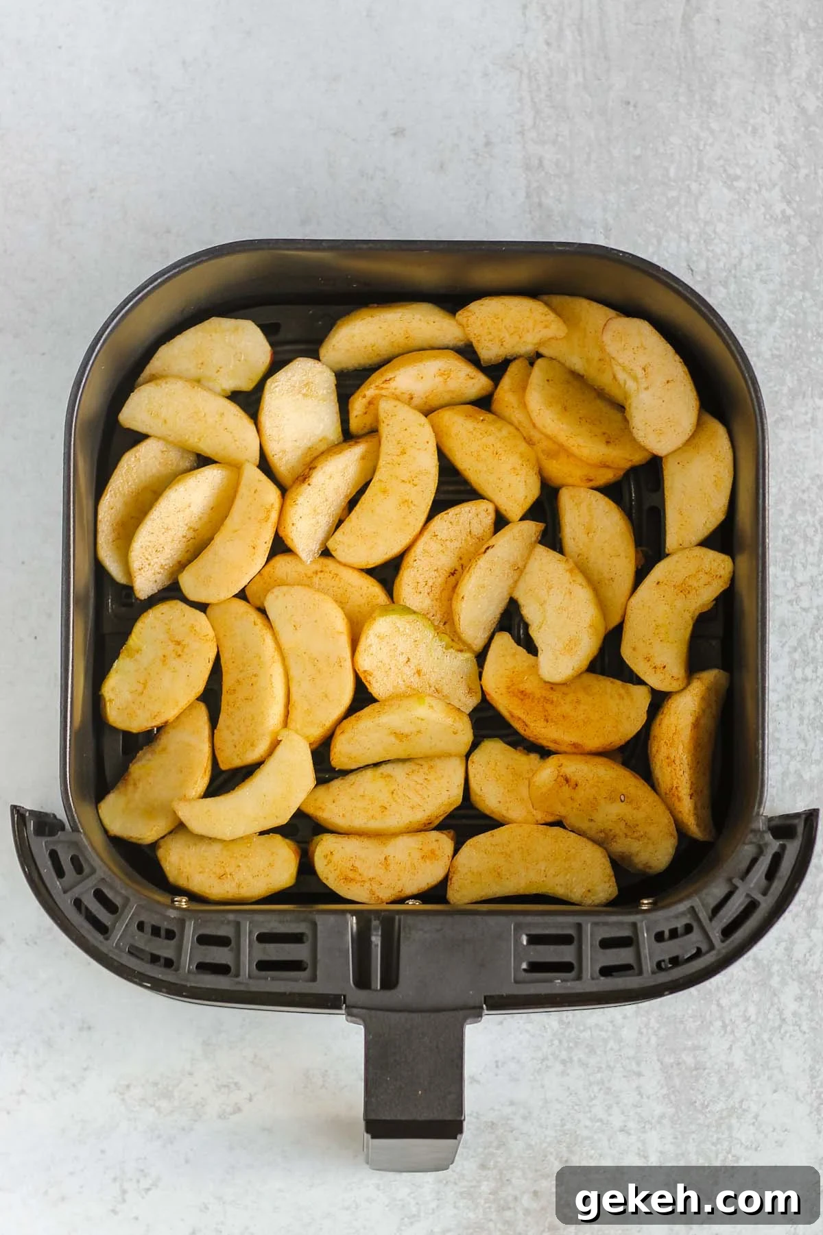 Apple slices with cinnamon laid out in an air fryer basket.