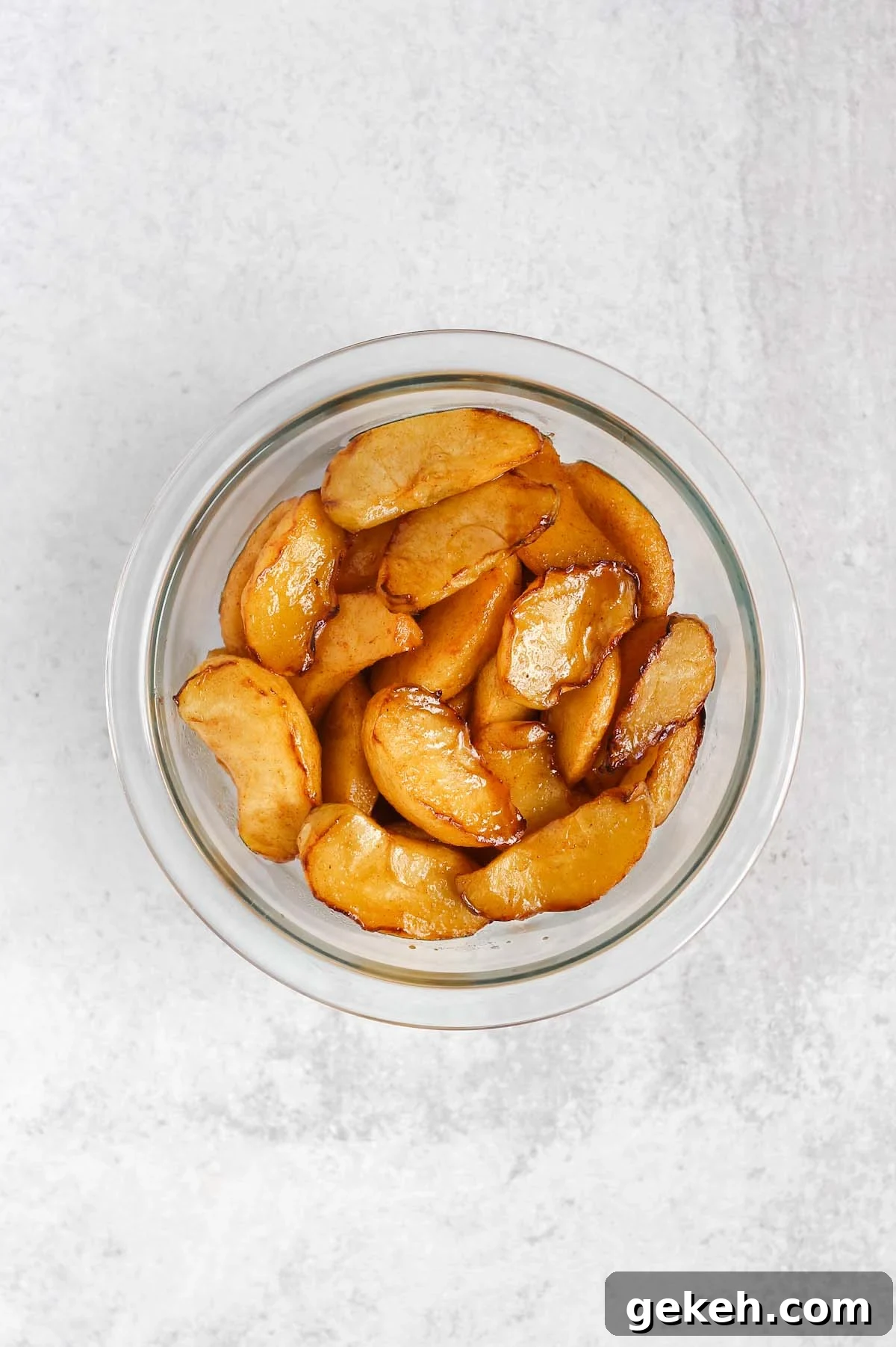 Air fried apple slices tossed with syrup/sugar mix in a glass mixing bowl.