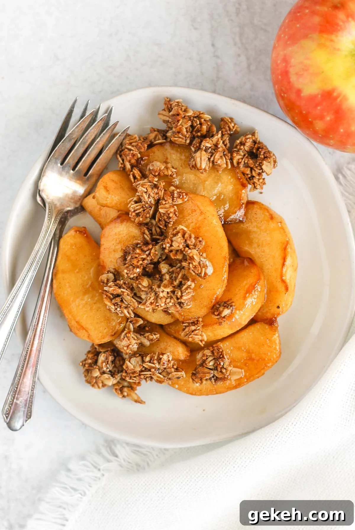 Air fried apples topped with granola on a white plate with two vintage forks on the plate with an apple off to the side.