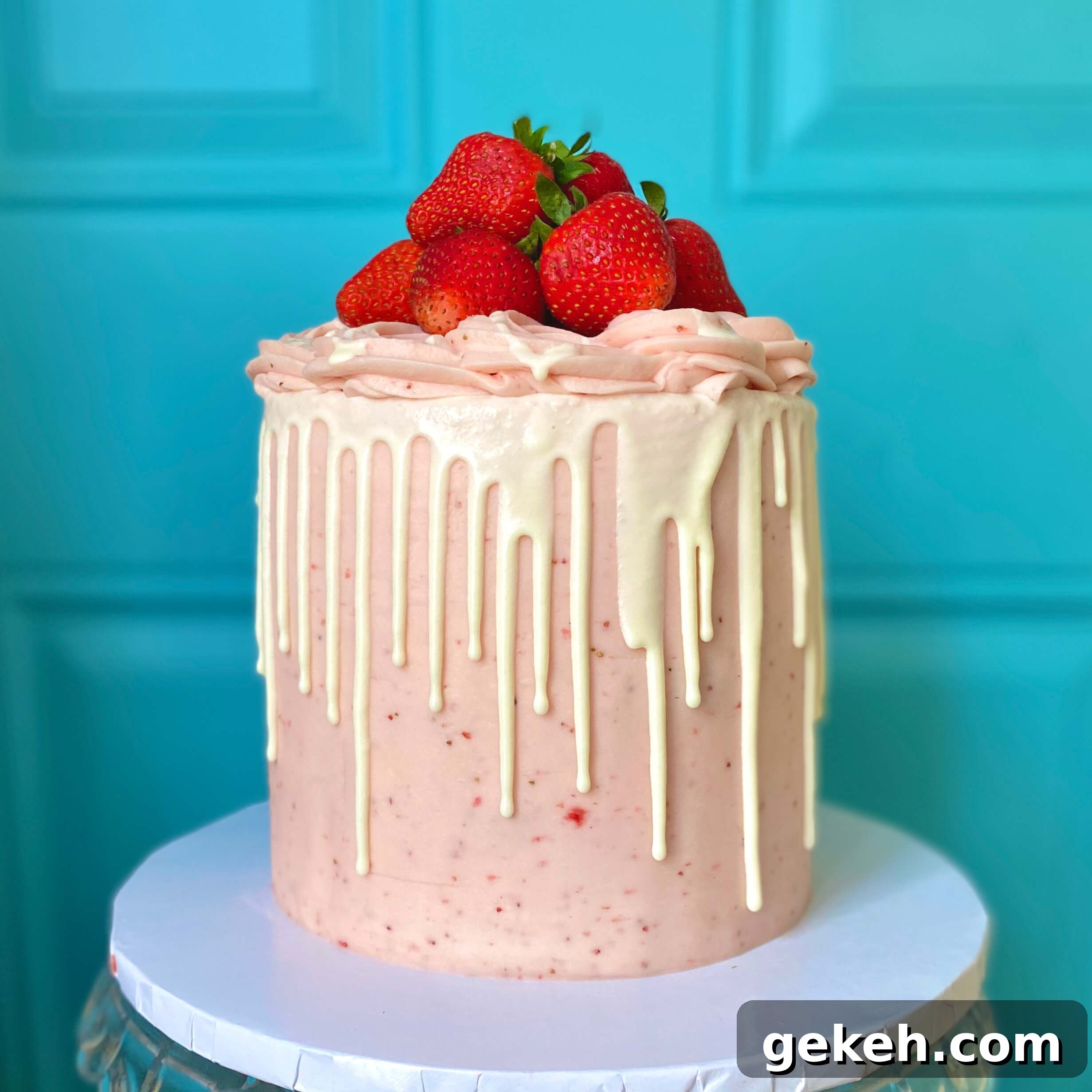 Bakery-Style Strawberry Buttercream Frosting Recipe 5 side view of a tall 6 inch strawberry cake with strawberry buttercream, white chocolate ganache drip, and a pile of fresh strawberries on top.