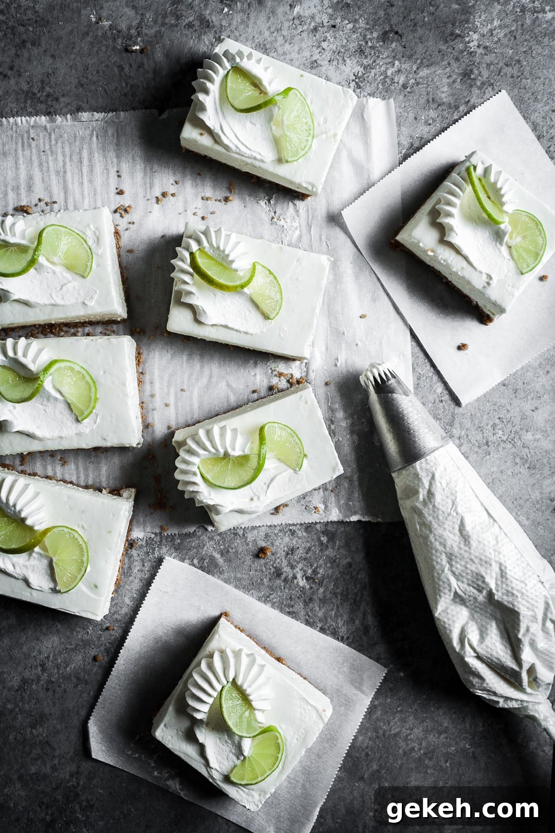 No-Bake Key Lime Cheesecake Bars Recipe for Zesty Dessert 12 Top view of sliced cheesecake bars on parchment paper squares on a grey background with a piping bag of whipped cream nearby