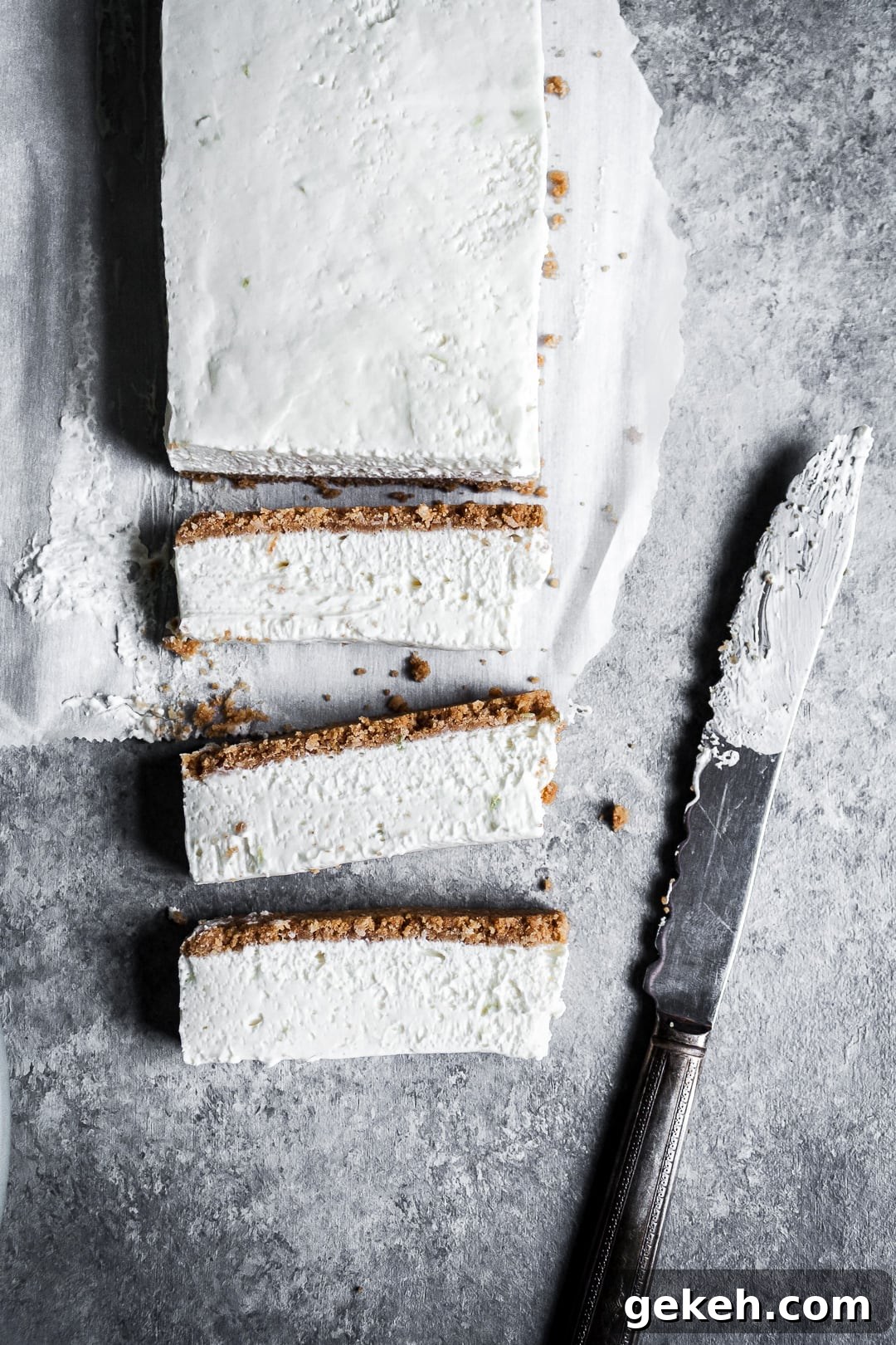 No-Bake Key Lime Cheesecake Bars Recipe for Zesty Dessert 3 Key Lime Cheesecake Bars seen from above with three slices laying on their side next to a vintage knife on a grey background