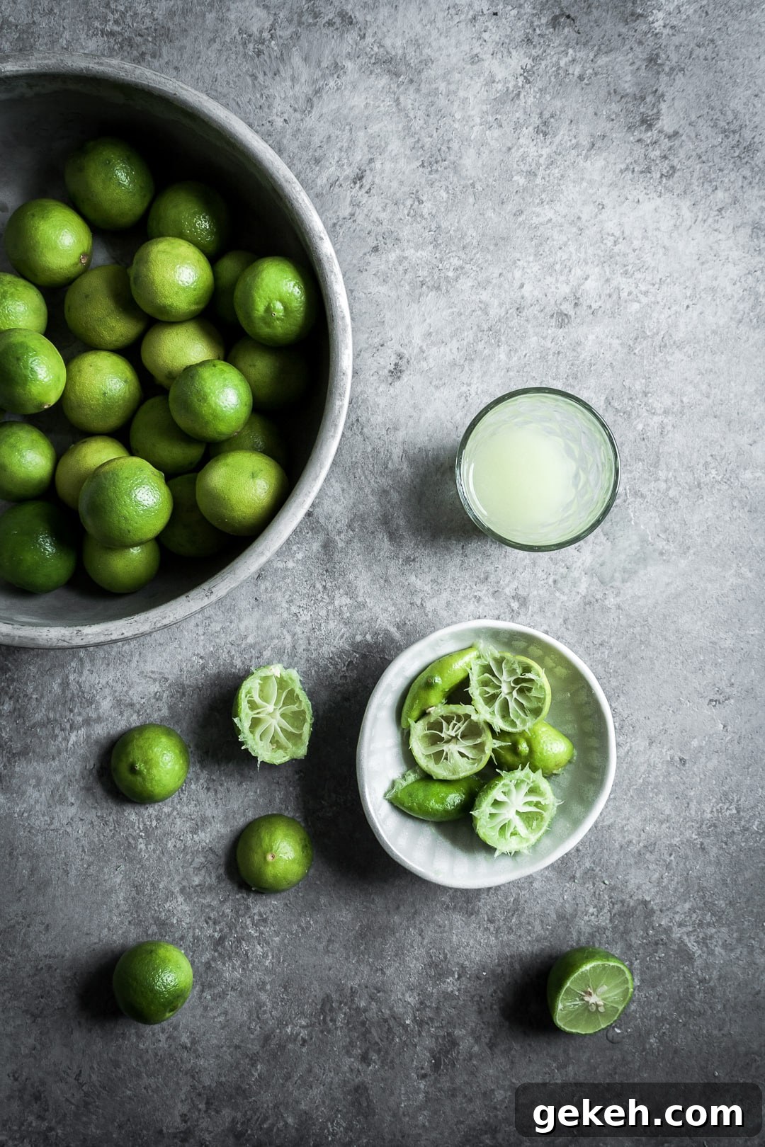 No-Bake Key Lime Cheesecake Bars Recipe for Zesty Dessert 4 Key limes in a bowl, some cut in half and squeezed, with a glass of key lime juice on a grey background