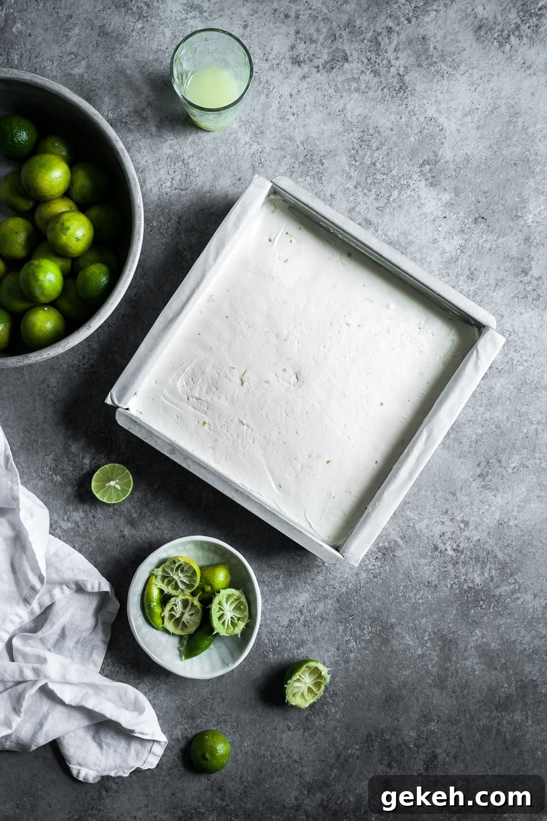No-Bake Key Lime Cheesecake Bars Recipe for Zesty Dessert 5 Pan of cheesecake bars on a grey background surrounded by key limes and a white linen napkin