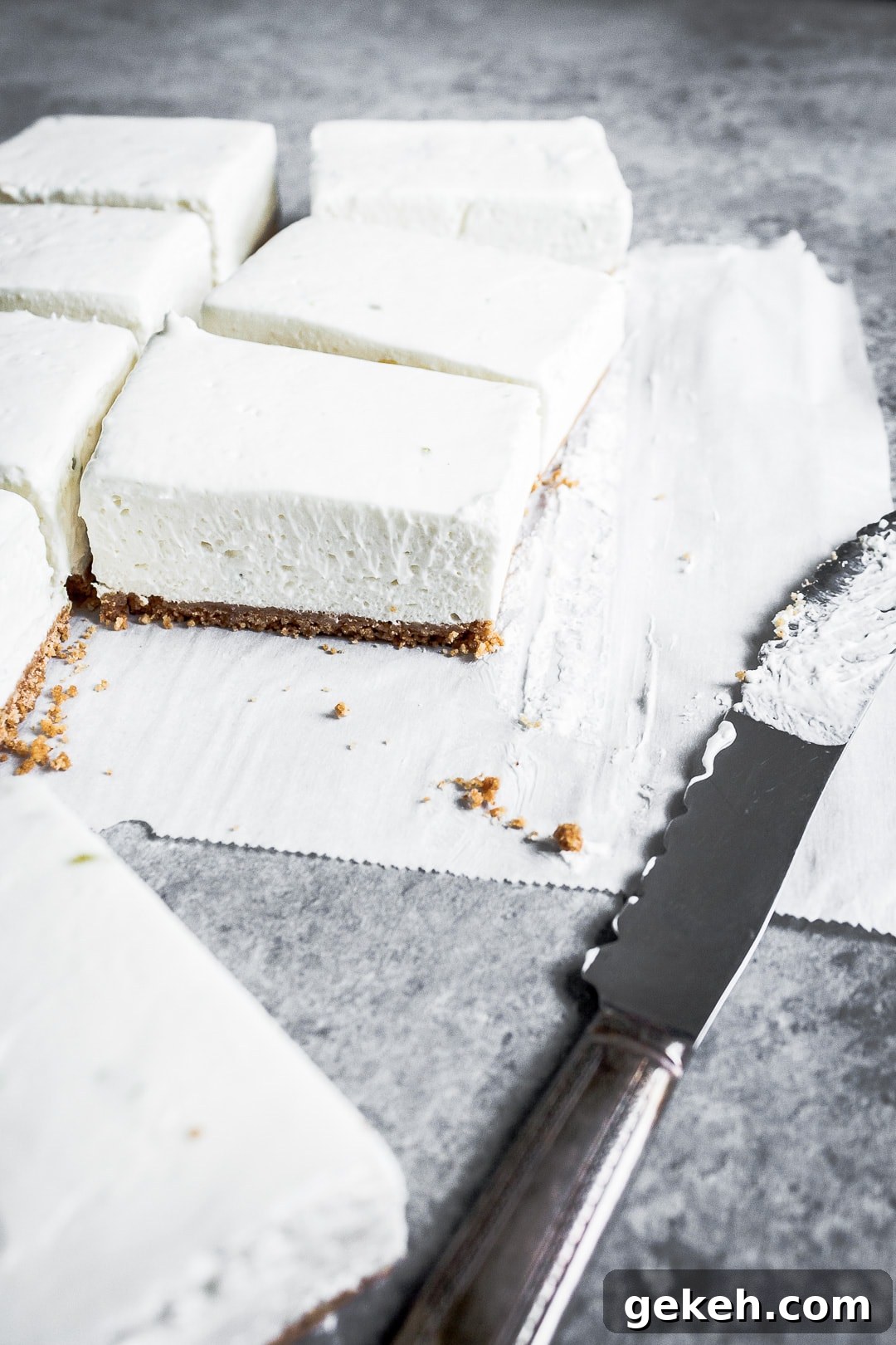 No-Bake Key Lime Cheesecake Bars Recipe for Zesty Dessert 6 45 degree angle view of sliced cheesecake bars on parchment paper squares on a grey background with a vintage knife nearby
