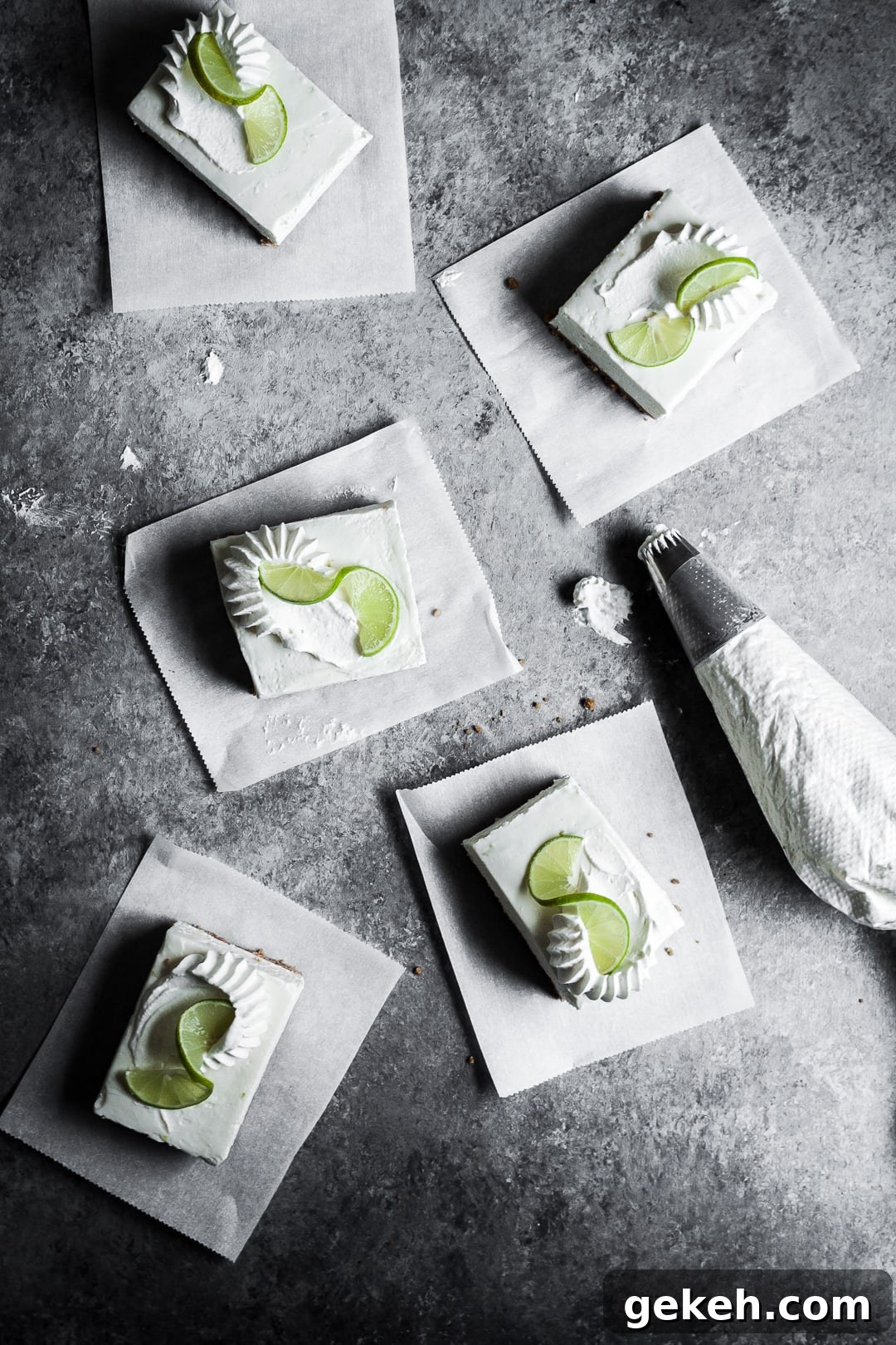 No-Bake Key Lime Cheesecake Bars Recipe for Zesty Dessert 10 Five sliced cheesecake bars on parchment paper squares on a grey background with a piping bag of whipped cream nearby